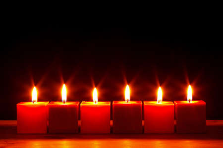 Still life photo of six square red candles burning bright against a black background.の写真素材