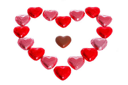 A heart made out of foil wrapped chocolates with an unwrapped one in the middle, white background.の写真素材