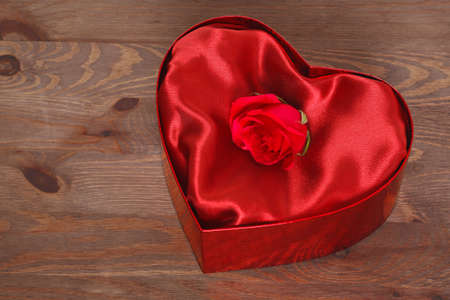 A single red rose in a heart shaped box with red satin lining against a rustic wooden background.の写真素材