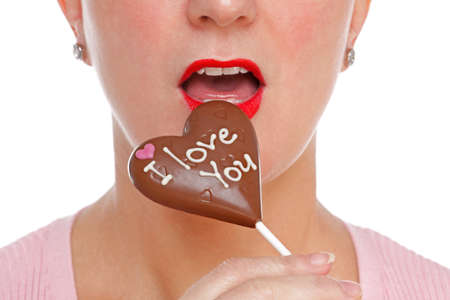 A woman wearing red lipstick about to eat a chocolate heart lollypop with the words I LOVE YOU upon...