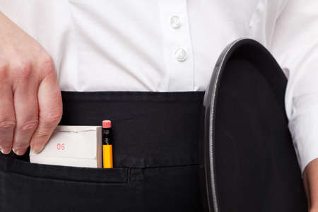 Close up of a waitress taking her order pad out of her apron pocket whilst she holds a tray in the other hand.の写真素材