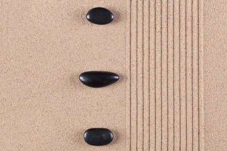 Three black pebbles on a raked sand zen garden.の写真素材