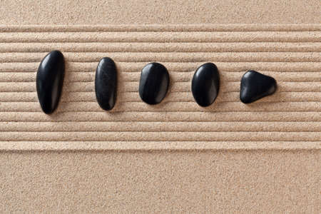 Five black pebbles on a raked sand zen garden.の写真素材