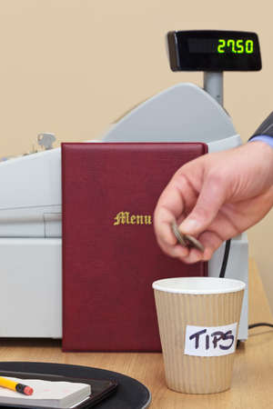A man dropping some coins into the tip cup at a restaurant after a meal.