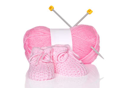 Baby girl knitted booties with pink wool and knitting needles, isolated on a white background.の写真素材