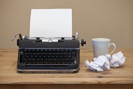 An old retro typewriter with a piece of blank paper for you to add your own text, coffee mug and two pieces of screwed up paper besides it on the desk.の写真素材