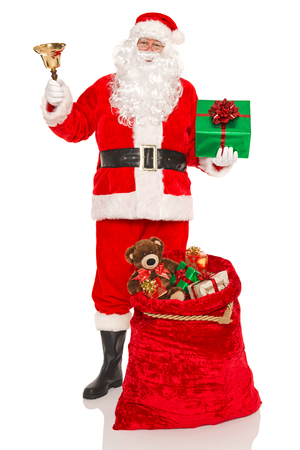 Santa Claus or Father Christmas with a sack full of gifts and holding a bell and gree presnt, isolated on a white background.の写真素材