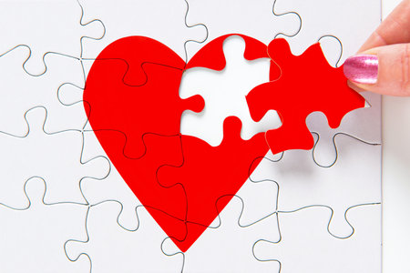 A woman putting the missing piece of a jigsaw red heart in place, good image to represent a love, broken heart, heartbreak, romance or Valentines theme.の写真素材