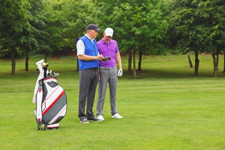 Golfer and caddy standing on the fairway of a par 4 looking at a course guide.の写真素材