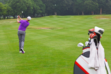 A golfer playing a mid iron fairway shot into the green on a par 4 hole, series of 3. Focus is on the golfer.の写真素材