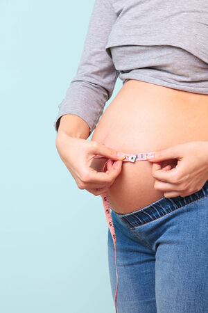 Photo of a 32 week preganant woman measuring her belly with a tape measure.