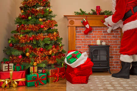 Santa Claus delivering gift wrapped presents under the tree on Christmas Eve with a sack full of toys for good girls and boys.の写真素材