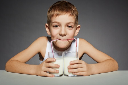 Boy drinking milk from two glassesの写真素材