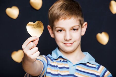 Portrait of boy holding gold heart on dark backgroundの写真素材