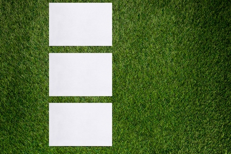 Three white sheets of paper lying on green grassの写真素材