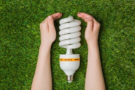 Hands with energy saving eco lamp over grassの写真素材