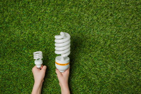 Hands with big and small energy saving lamps over grassの写真素材