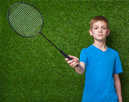 Boy holding badminton racket over green grassの写真素材