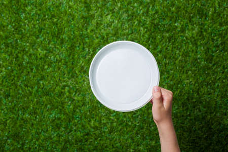 Human hand holding empty dish over green grassの写真素材