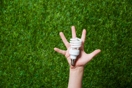 Human hand holding energy saving lamp over green grassの写真素材
