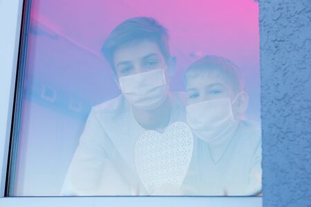 Children wearing protective masks loking through the window of hospitalの写真素材