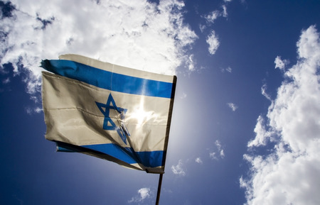 Old Israeli flag waving at sunny day on blue sky backgroundの写真素材
