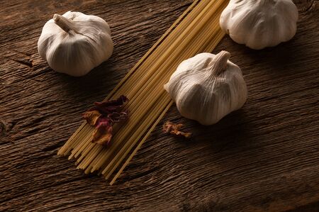 Three garlic heads with spaghetti on a barn woodの写真素材