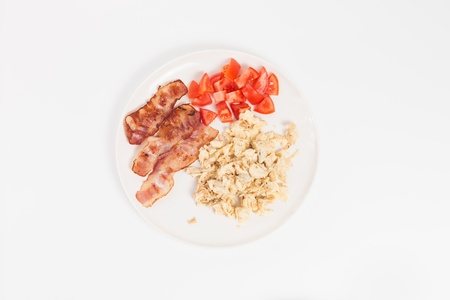 fried eggs with bacon and vegetables on white backgroundの写真素材