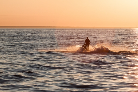 Young guy cruising in the baltic sea  on a jet ski during sunsetの写真素材