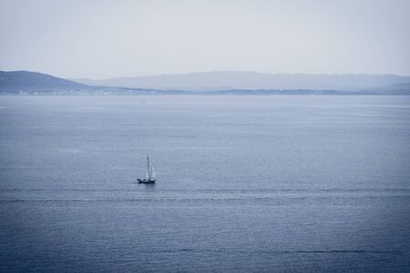 Lonely sailboat in sea and mountains at backgroundの写真素材
