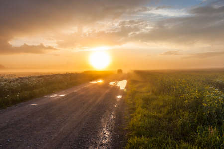 Car on the rural foggy road going to the sunsetの写真素材