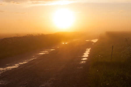 Misty rural road with puddles in the fieldの写真素材