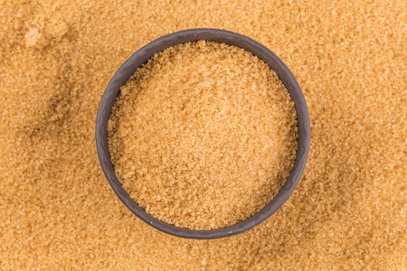 brown sugar in dark bowl on a background of sugarの写真素材