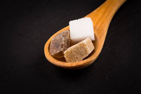 White refined and brown sugar in wooden spoon on dark stone backgroundの写真素材