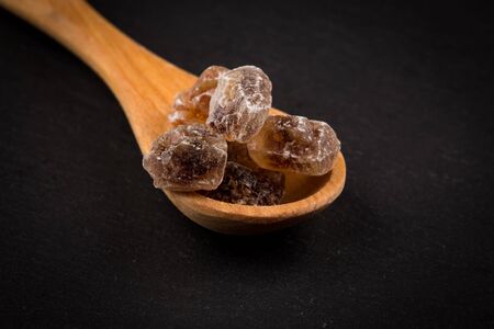 caramelized candy brown sugar in wooden spoon on a dark stone boardの写真素材