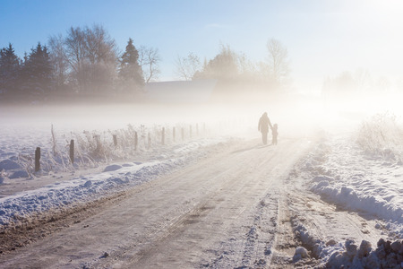 Mother and child on foggy snow road near farmの写真素材