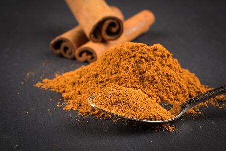 cinnamon sticks with powder on spoon on dark stone plateの写真素材