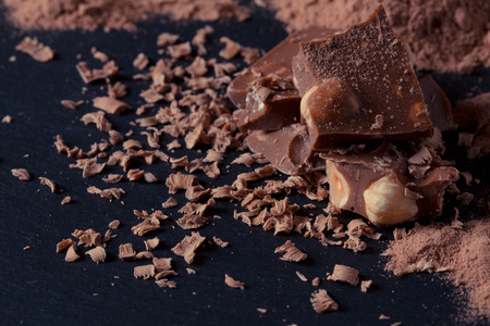 Broken chocolate nuts pieces and cocoa powder on dark background