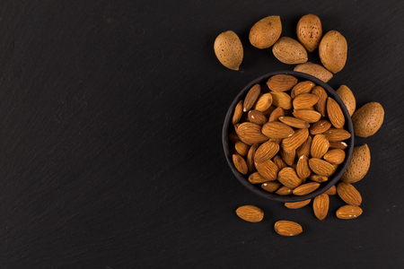 Pile of almonds nuts in a stone bowl on a dark black backgroundの写真素材