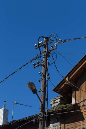old wires on electric pole over blue sky and old houseの写真素材