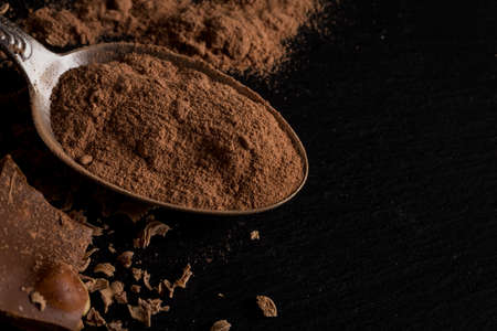 Broken chocolate nuts pieces and cocoa powder in spoon on dark backgroundの写真素材