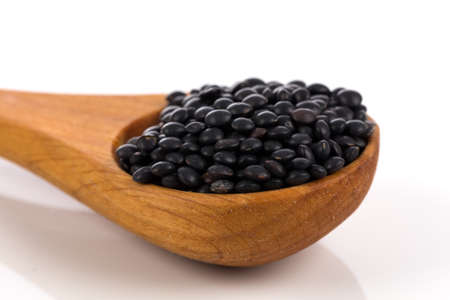 Black organic lentils in wooden spoon isolated on white backgroundの写真素材