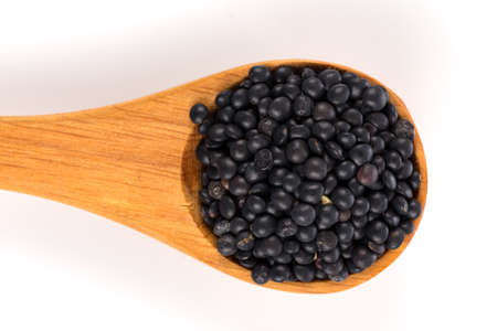 Black organic lentils in wooden spoon isolated on white backgroundの写真素材