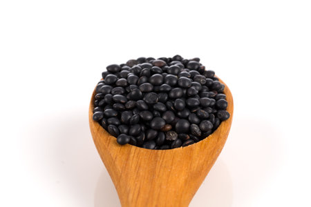 Black organic lentils in wooden spoon isolated on white backgroundの写真素材