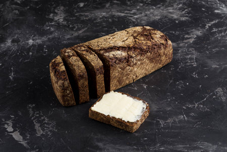 Rye black bread with seeds  and butter on dark board background