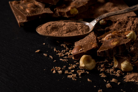 Broken chocolate nuts pieces and cocoa powder in spoon on dark backgroundの写真素材