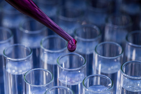 Laboratory glassware with pipette dropping red pink fluid into test tubeの写真素材