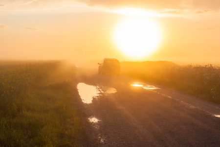 Car on rural road with fog and sunsetの写真素材