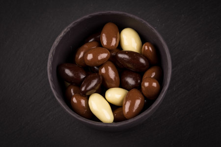 almonds in white, dark, milk chocolate in a bowl on stone boardの写真素材