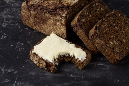 Rye black bread with seeds  and butter on dark board backgroundの写真素材